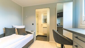 A modern hotel room with a bed, a desk, and a shower area. - Palenque - Apartment Palenque (Sylt-Ost)