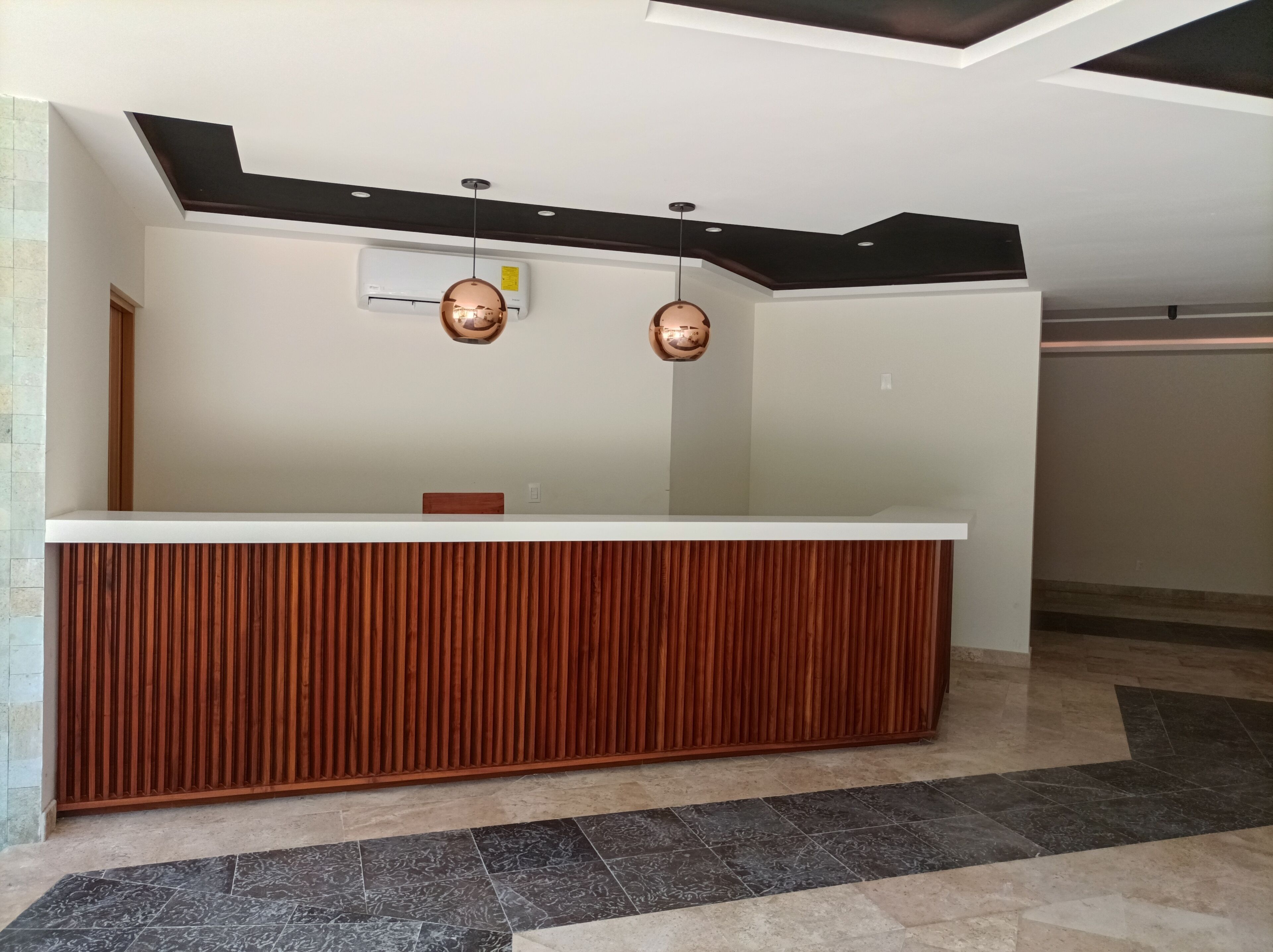 A reception desk with a wooden panel design, a ceiling with recessed lighting, and an air conditioning unit mounted on the wall.