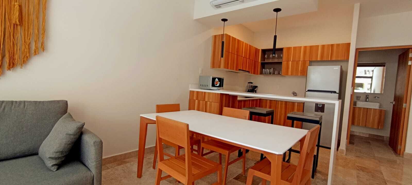 Cocina compacta con armarios de madera, encimera blanca y refrigerador empotrado.
