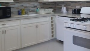Een keuken met witte kastjes, een magnetron, een fornuis en een betegelde spatwand.