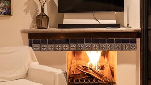 A cozy living room with a fireplace, a flat-screen TV mounted above it, a white sofa, and a small table with a candle and book.