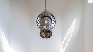 A spacious hallway with a high ceiling, a hanging chandelier, and a view into a living area with a sofa and a television.