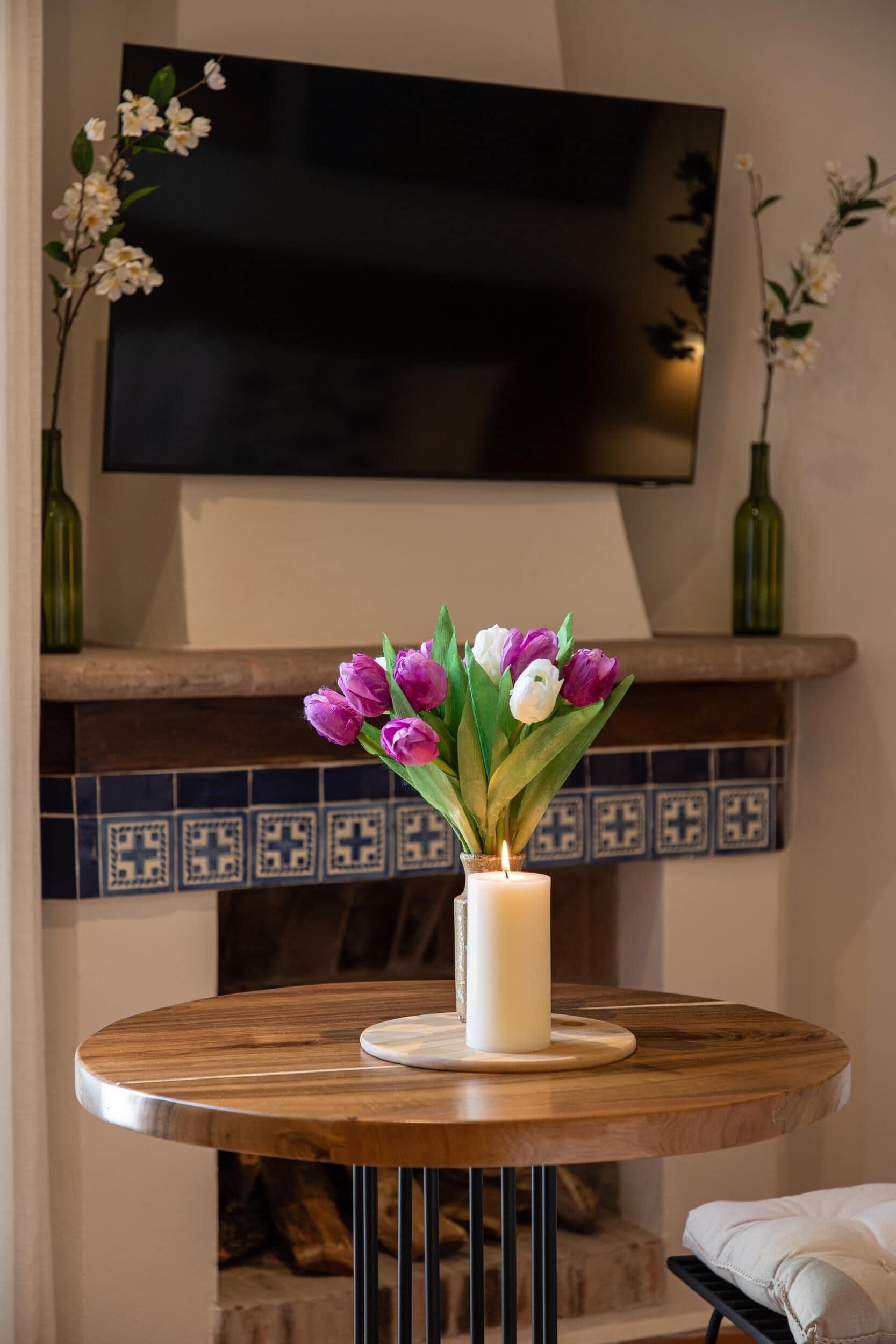 A round wooden table with a white candle and a bouquet of purple and white tulips.