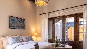 A bedroom with a bed, a table with chairs, a chandelier, and a window with curtains.