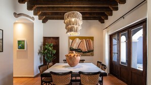A dining area with a large table, six wicker chairs, a hanging light fixture, and a large vase.