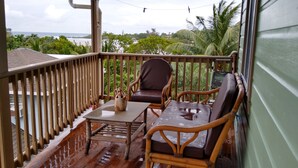 Eine Holzterrasse mit Tisch und zwei Korbstühlen, mit Blick auf einen Strand und Palmen.