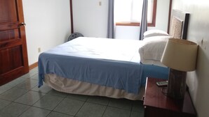 Ein Schlafzimmer mit einem Bett, einem Nachttisch, einer Lampe, einem Fenster mit Vorhängen und einer Tür.