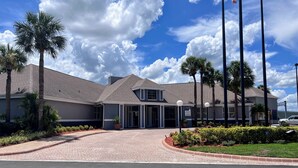 A hotel with a modern architectural design, featuring a large entrance with a covered walkway, palm trees, and a clear blue sky.