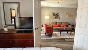 A hotel room with a bed, a TV, a dresser, and a living area with a sofa and a coffee table.