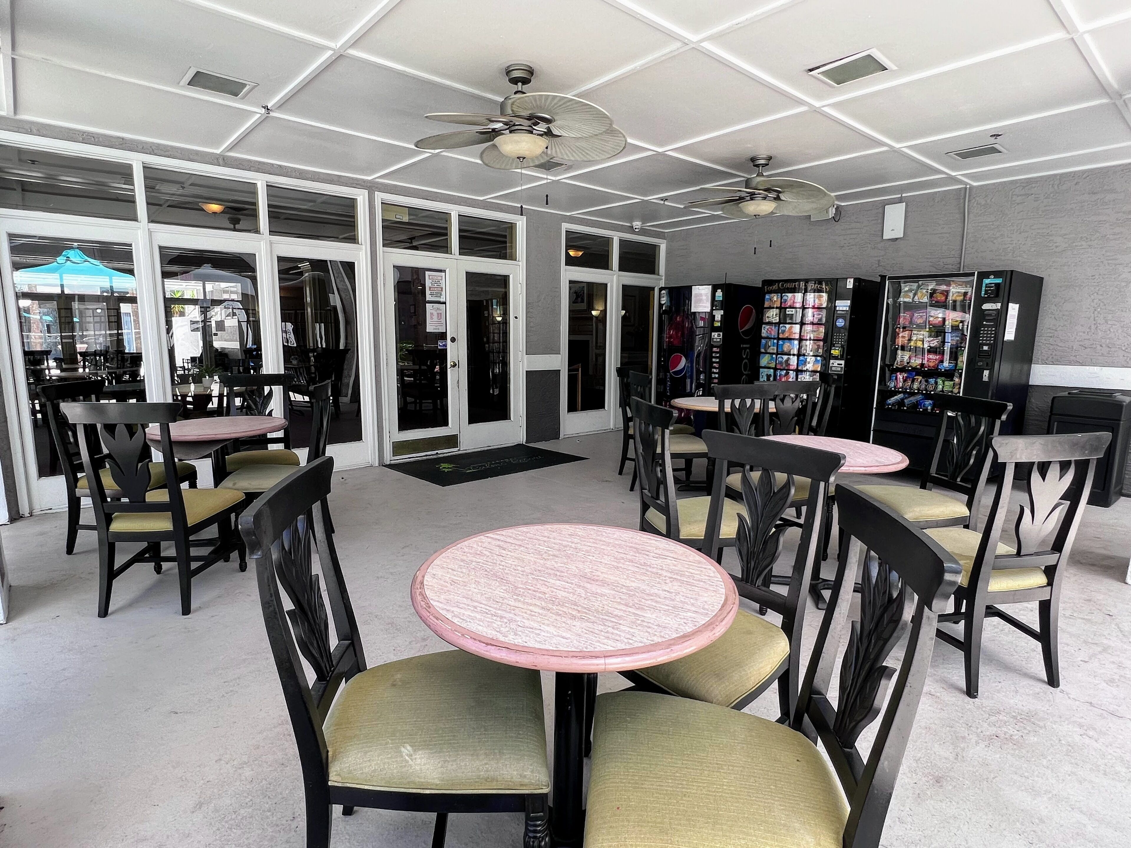 L’intérieur d’un restaurant avec des tables et des chaises rondes, des ventilateurs de plafond et des distributeurs automatiques.