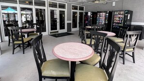 A restaurant interior with round tables and chairs, ceiling fans, and vending machines.