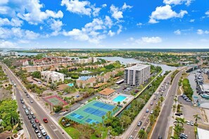 Un paysage urbain côtier avec un hôtel imposant, doté de plusieurs étages, d’une piscine et d’un court de tennis.