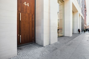 A modern building facade with a large wooden door marked with the number 44, a clean, tiled ground floor, and a pedestrian walkway.