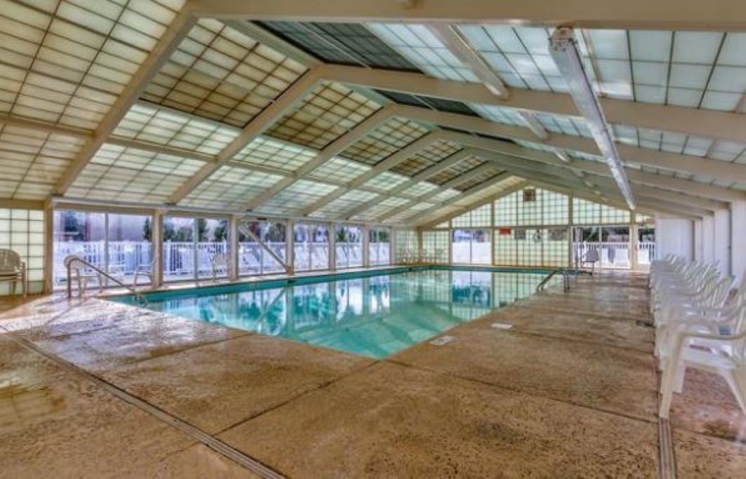An indoor swimming pool with a glass ceiling, clear pool water, and a tiled floor.