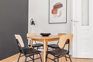 A dining area with a round wooden table, four chairs, a black bowl, and a framed abstract painting on the wall.