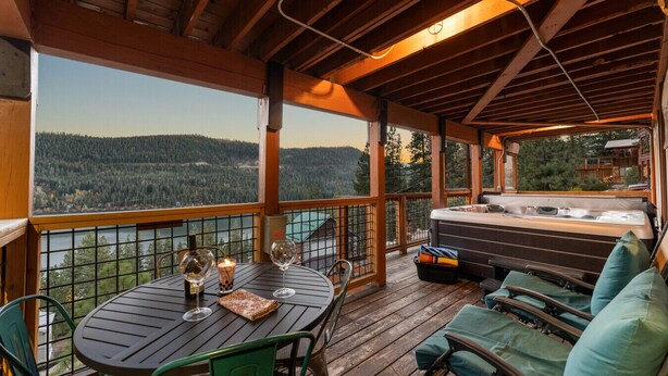 A wooden deck with a hot tub, seating area, and a table with wine glasses and a candle.