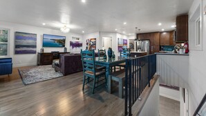 A spacious living area with a dining table, chairs, and a sofa. There is a kitchen area with cabinets and appliances.