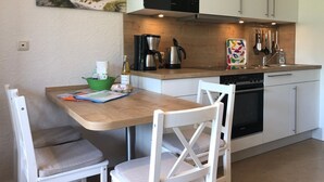 A compact kitchen with a wooden table, white chairs, a coffee maker, a kettle, and a microwave.