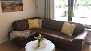 A living room with a brown leather sofa, a white coffee table, and a painting of a beach scene.