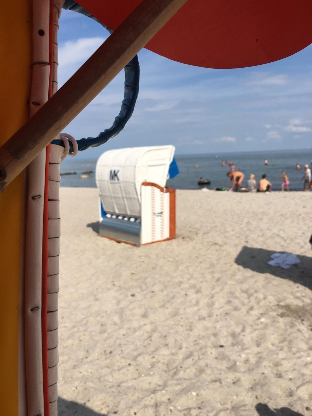 A beach with a white beach chair and a blue umbrella.