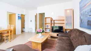 A modern living room with a brown sofa, a wooden coffee table, a flat-screen TV, and a bookshelf. - Apartment No.3 - Seestern - Ferienhof Kluvetasch (Neustadt in Holstein)