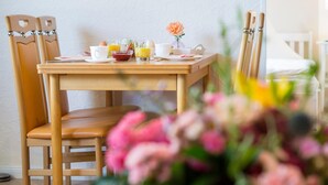 A wooden dining table with chairs, a vase with flowers, and breakfast items. - Apartment No.3 - Seestern - Ferienhof Kluvetasch (Neustadt in Holstein)
