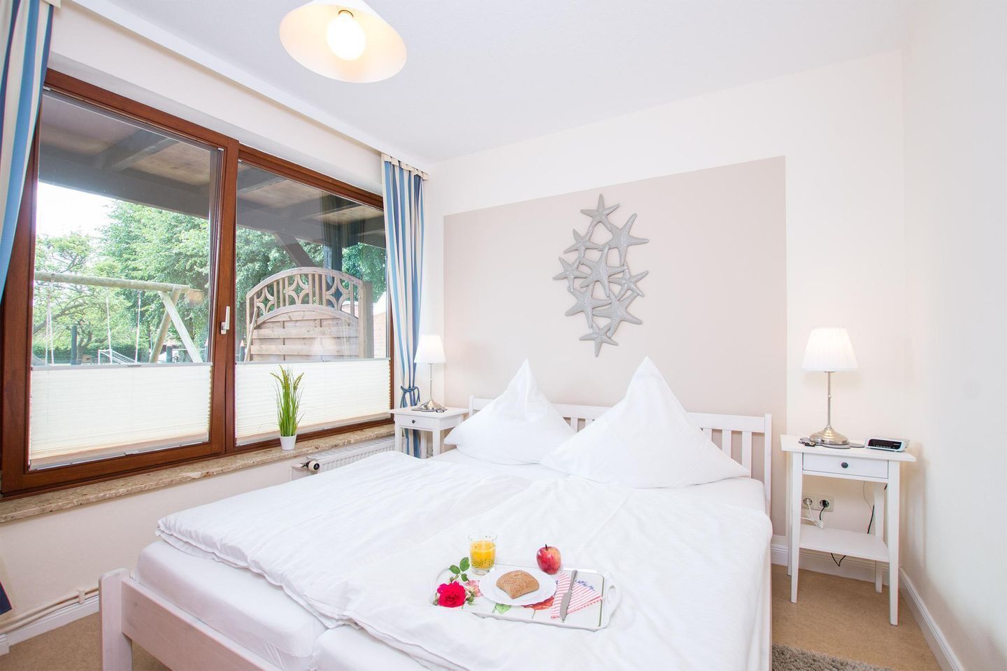 A hotel room with a bed, a bedside table with a lamp, a window with curtains, and a decorative wall piece.