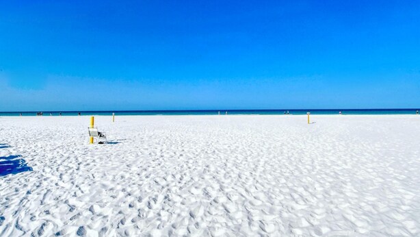 Une vaste plage de sable blanc, avec un ciel bleu clair et une mer d’un bleu limpide.
