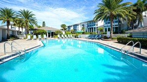 Une piscine d’un bleu éclatant, entourée de chaises longues et de palmiers, avec un bâtiment en arrière-plan.