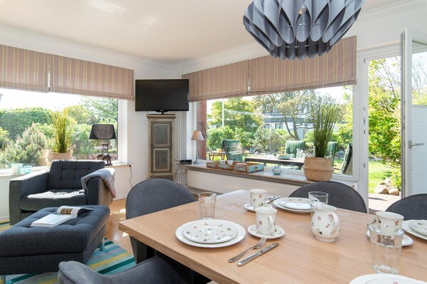 A modern living room with a dining area, large windows, and a view of the garden.