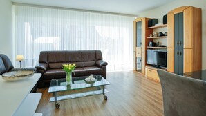 A modern living room with a leather sofa, a glass coffee table, and a wooden cabinet with a television. - Risgap - Schmidtpott - Cozy 3-room apartment for 4 persons with terrace (Wenningstedt-Braderup (Sylt))