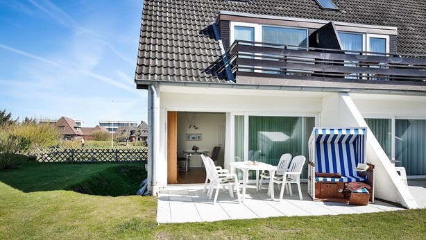 A modern house with a patio, a dining area, and a striped beach chair. - Risgap - Schmidtpott - Cozy 3-room apartment for 4 persons with terrace (Wenningstedt-Braderup (Sylt))