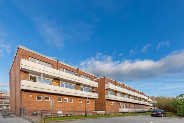 Un immeuble à plusieurs étages, doté d’une façade en briques, de balcons et d’un espace de stationnement.