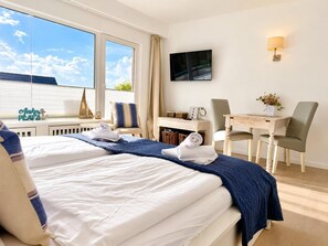 A hotel room with a large bed, a desk, two chairs, a TV, and a window with a view. - Seestern - Bright app. for 2 pers. - Balcony, parking space, WLAN. Pets (Wenningstedt-Braderup (Sylt))