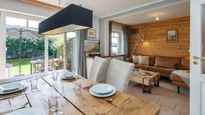A dining area with a wooden table set for four, a wicker chair, and a chessboard. - Am Sandwall Ostseite - House close to the beach for 4 persons with sauna, terrace, garden, (Sylt)