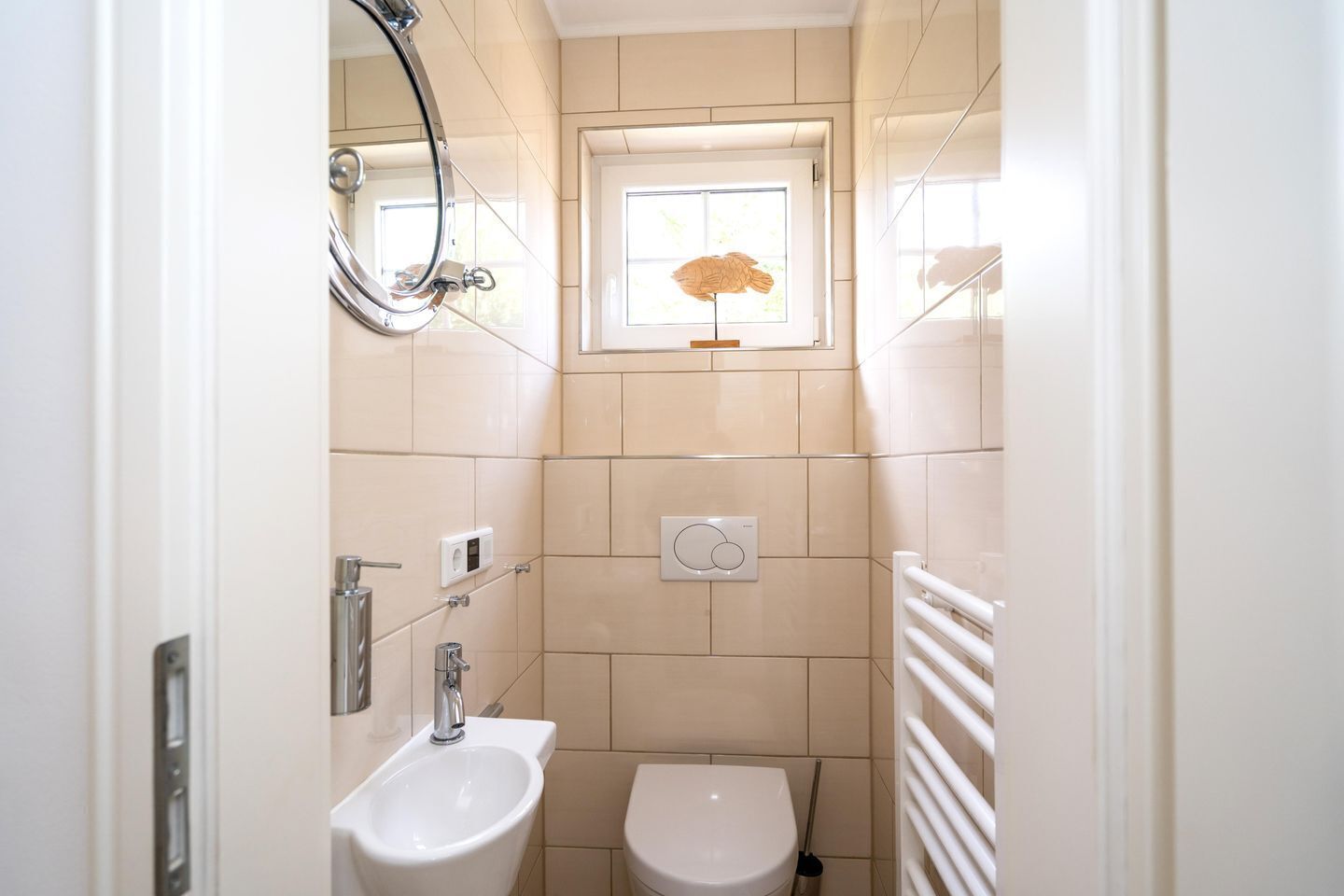 A small, modern bathroom with a toilet, sink, and a window with a decorative umbrella.