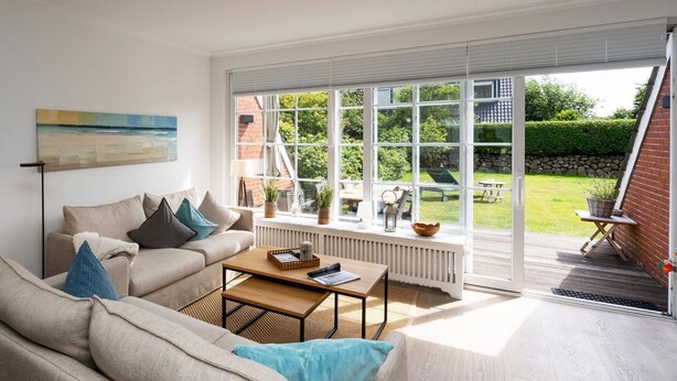 A modern living room with a sofa, coffee table, and a large window overlooking a garden.
