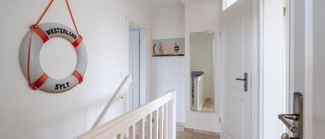 A hallway with a white door, a white railing, and a life preserver hanging on the wall.