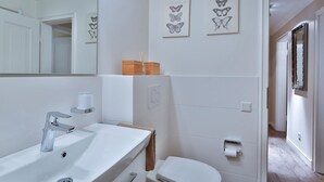 A modern bathroom with a white sink, mirror, and toilet. There are two framed butterfly artworks on the wall.