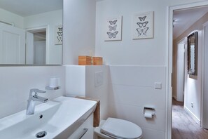 A modern bathroom with a white sink, mirror, and toilet. There are two framed butterfly artworks on the wall. - Apartment Pebbles - 3-room apartment for 4 persons with terrace, parking space, (Sylt)