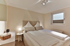 A bedroom with a bed, bedside tables, a lamp, a window, and a radiator. - Apartment Pebbles - 3-room apartment for 4 persons with terrace, parking space, (Sylt)