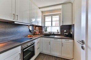 A modern kitchen with white cabinets, a stainless steel range hood, a built-in oven, and a window providing natural light. - Apartment Pebbles - 3-room apartment for 4 persons with terrace, parking space, (Sylt)
