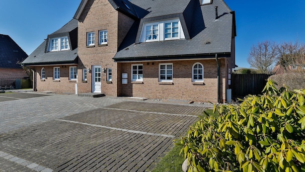 A two-story brick building with a steeply pitched roof, multiple windows, and a paved driveway.