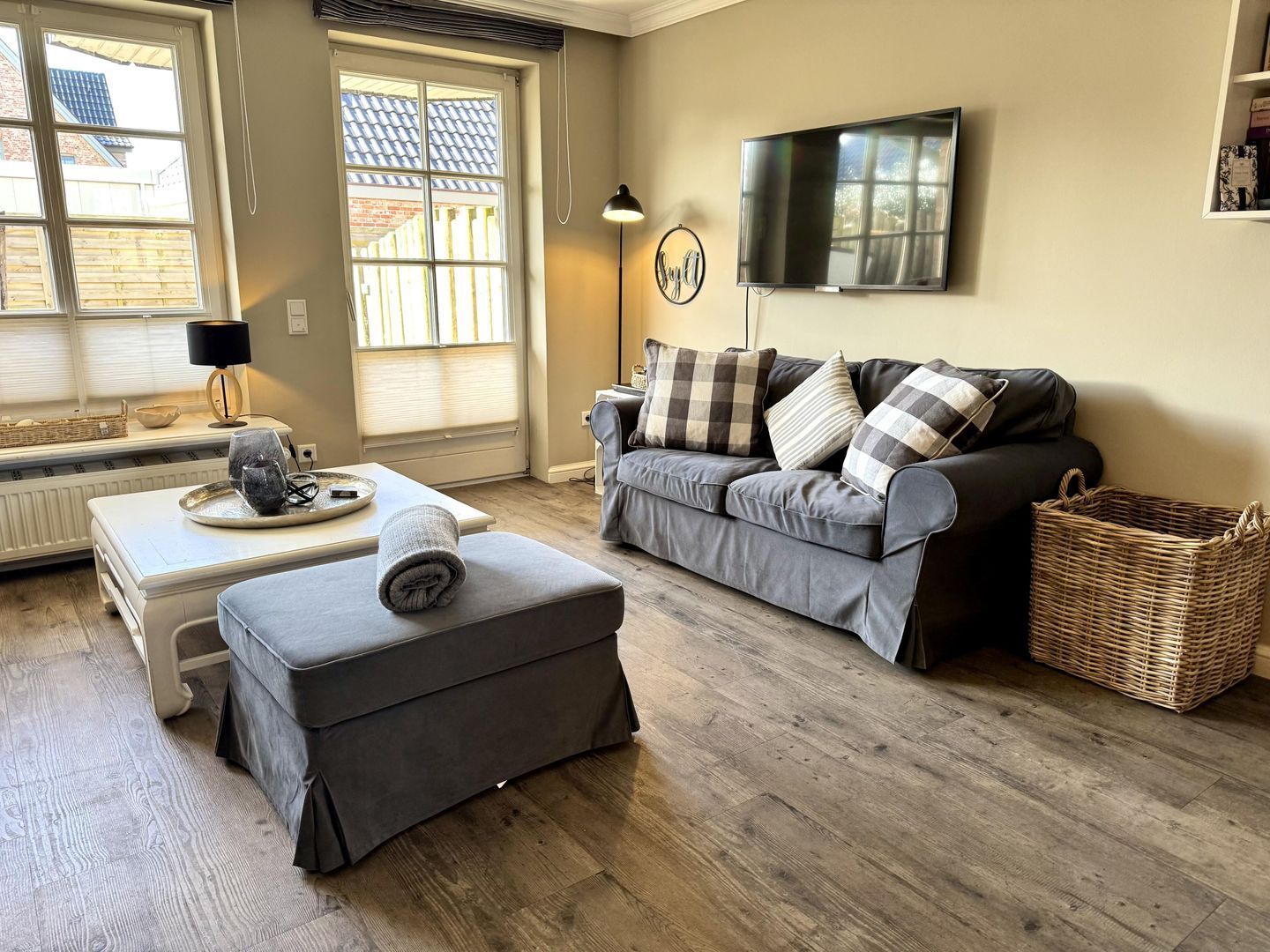 A living room with a sofa, ottoman, and a television on the wall.