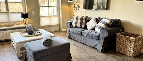 A living room with a sofa, ottoman, and a television on the wall.