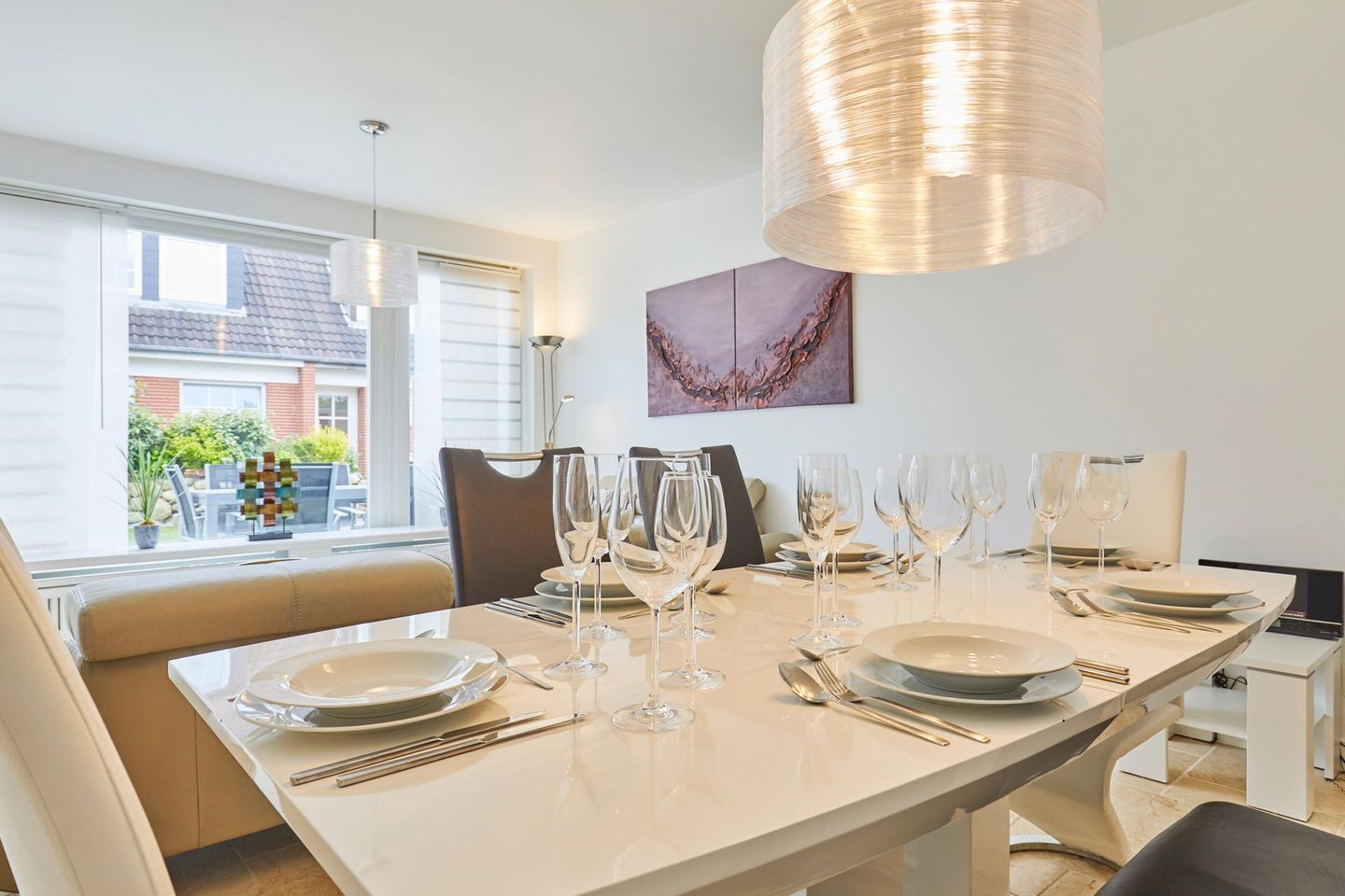 A modern dining area with a long table set for six, including wine glasses and cutlery.