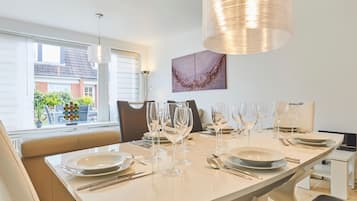 A modern dining area with a long table set for six, including wine glasses and cutlery.