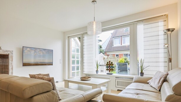 Ein modernes Wohnzimmer mit einem beigefarbenen Sofagarnitur, einem weißen Couchtisch und einem großen Fenster mit Jalousien.