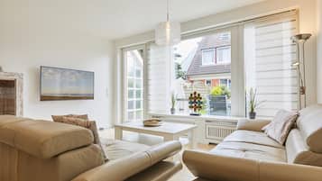 A modern living room with a beige sofa set, a white coffee table, and a large window with blinds.