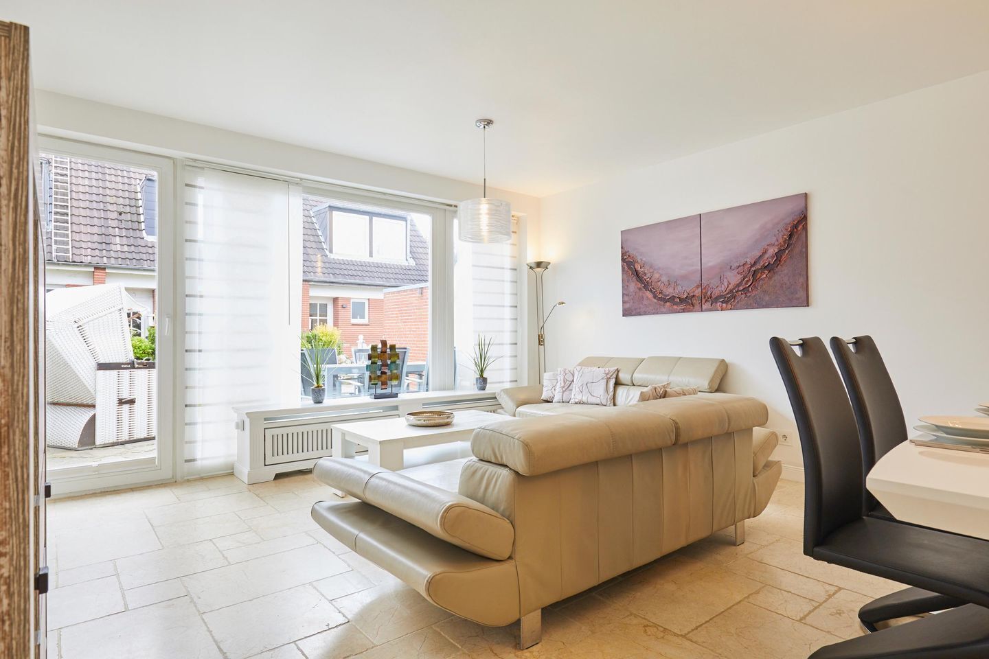 A modern living room with a beige sofa, a dining table with chairs, and a large window offering a view of the outside.